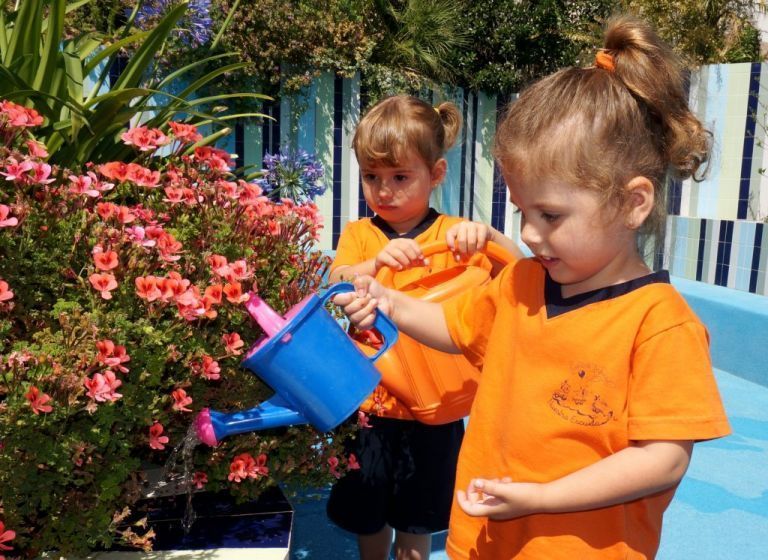 Dos niñas están regando flores con una regadera azul