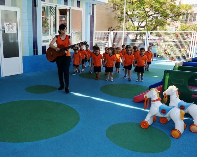 Una mujer toca una guitarra delante de un grupo de niños.
