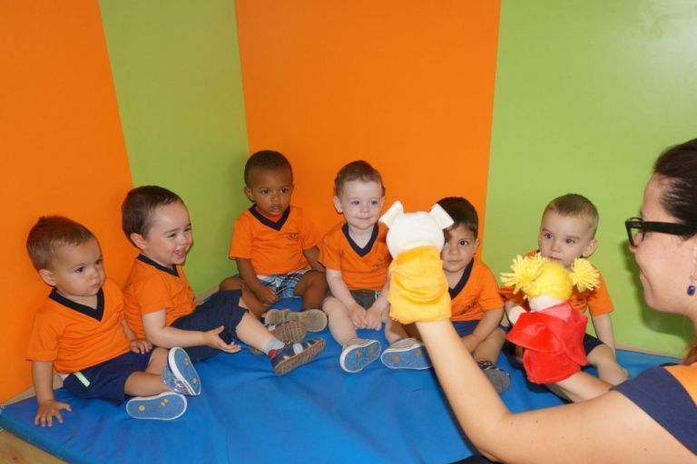 Una mujer sostiene una marioneta delante de un grupo de niños.