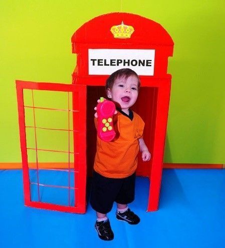 Un niño pequeño está parado en una cabina telefónica sosteniendo un teléfono de juguete.
