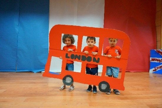 Tres niños están parados frente a un autobús de dos pisos de cartón que dice Londres.