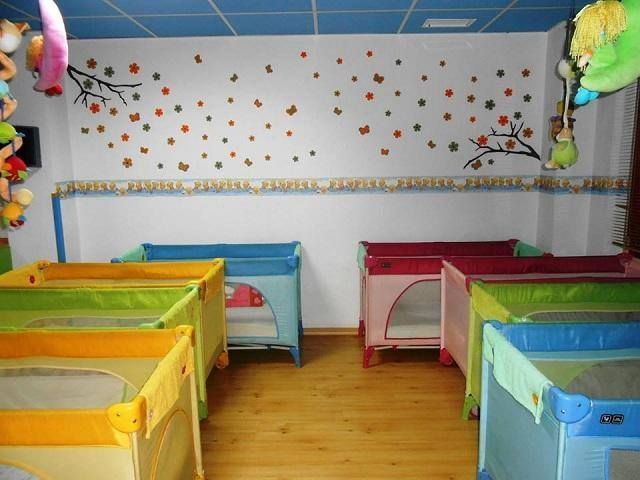 Una fila de cunas coloridas en una habitación con animales de peluche colgando del techo.