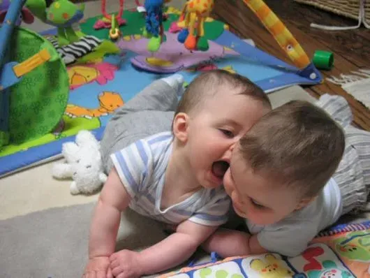 Dos bebés están acostados en el suelo jugando con juguetes.