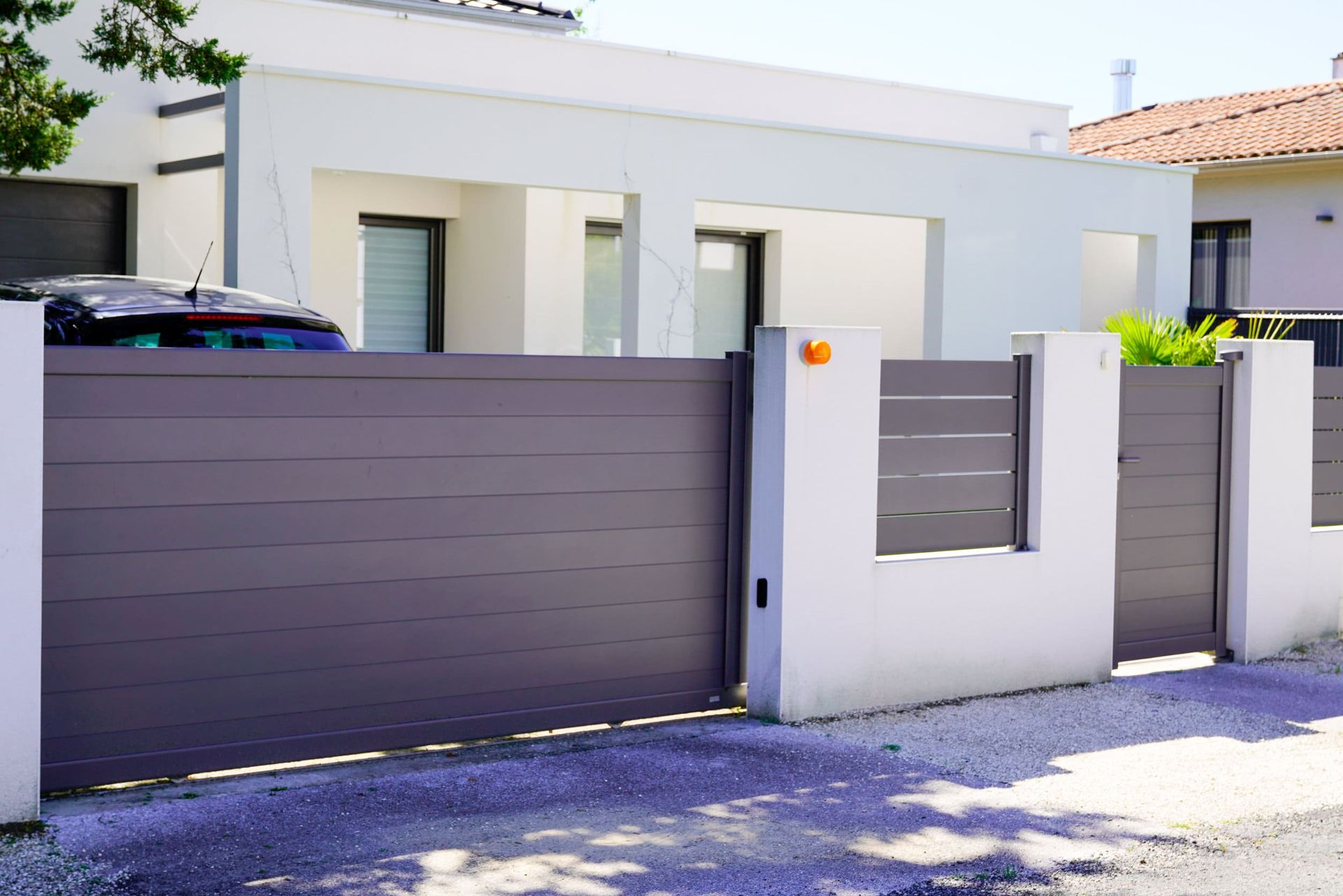 Puerta gris y valla delante de una casa blanca moderna con un coche en la entrada.