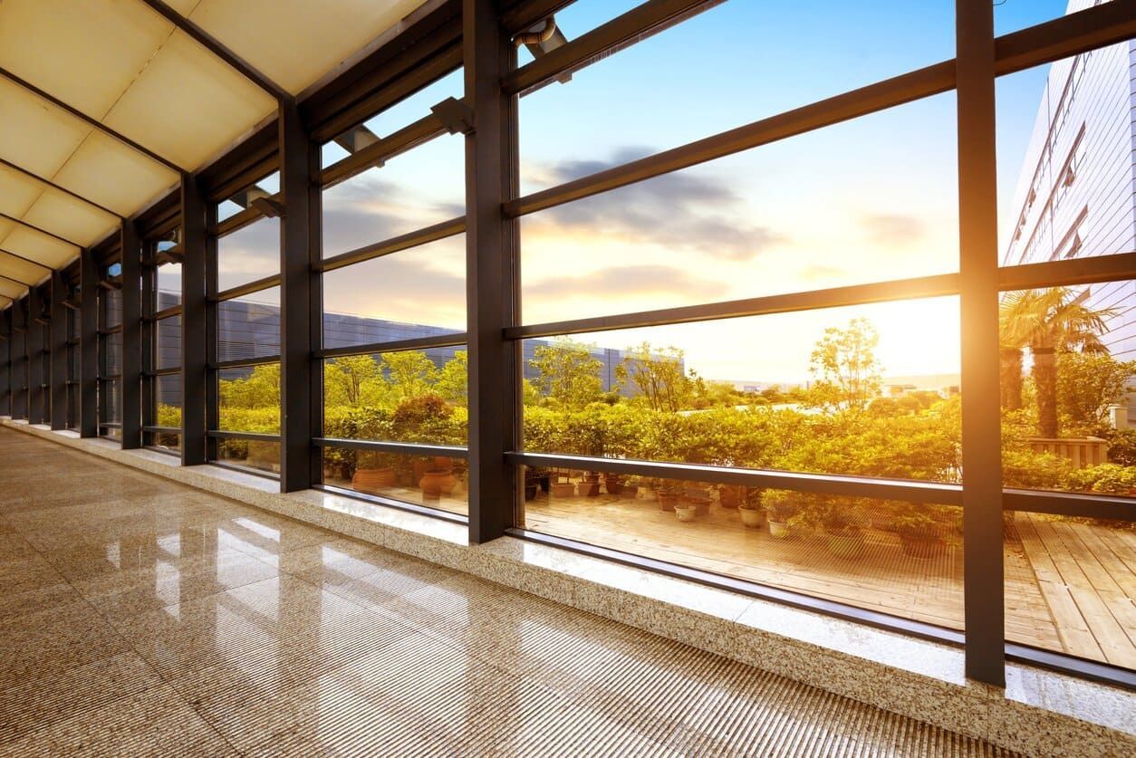 Pasillo con grandes ventanales con vistas a un soleado paisaje exterior.