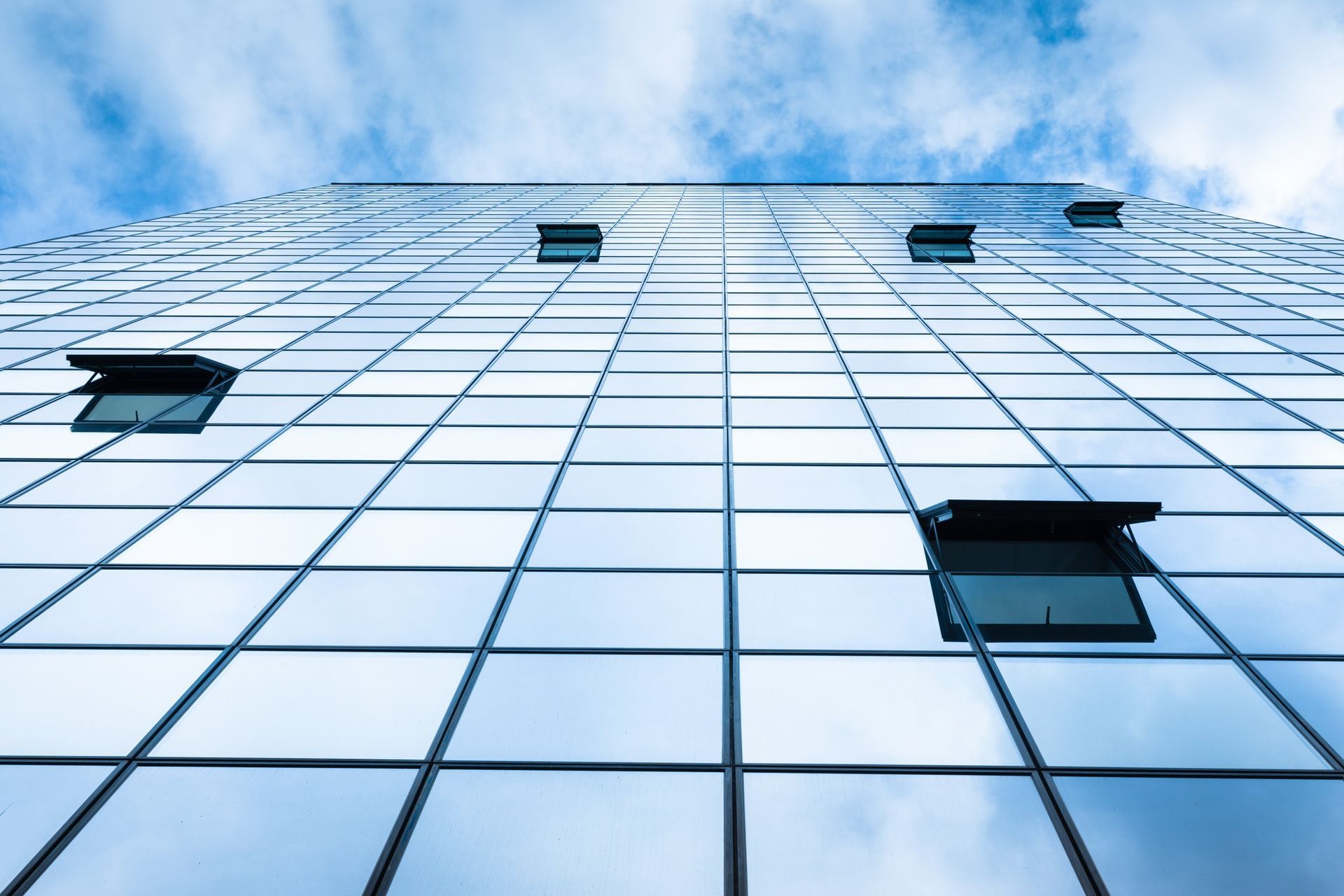Rascacielos con ventanas de vidrio que reflejan el cielo azul, algunas ventanas abiertas.