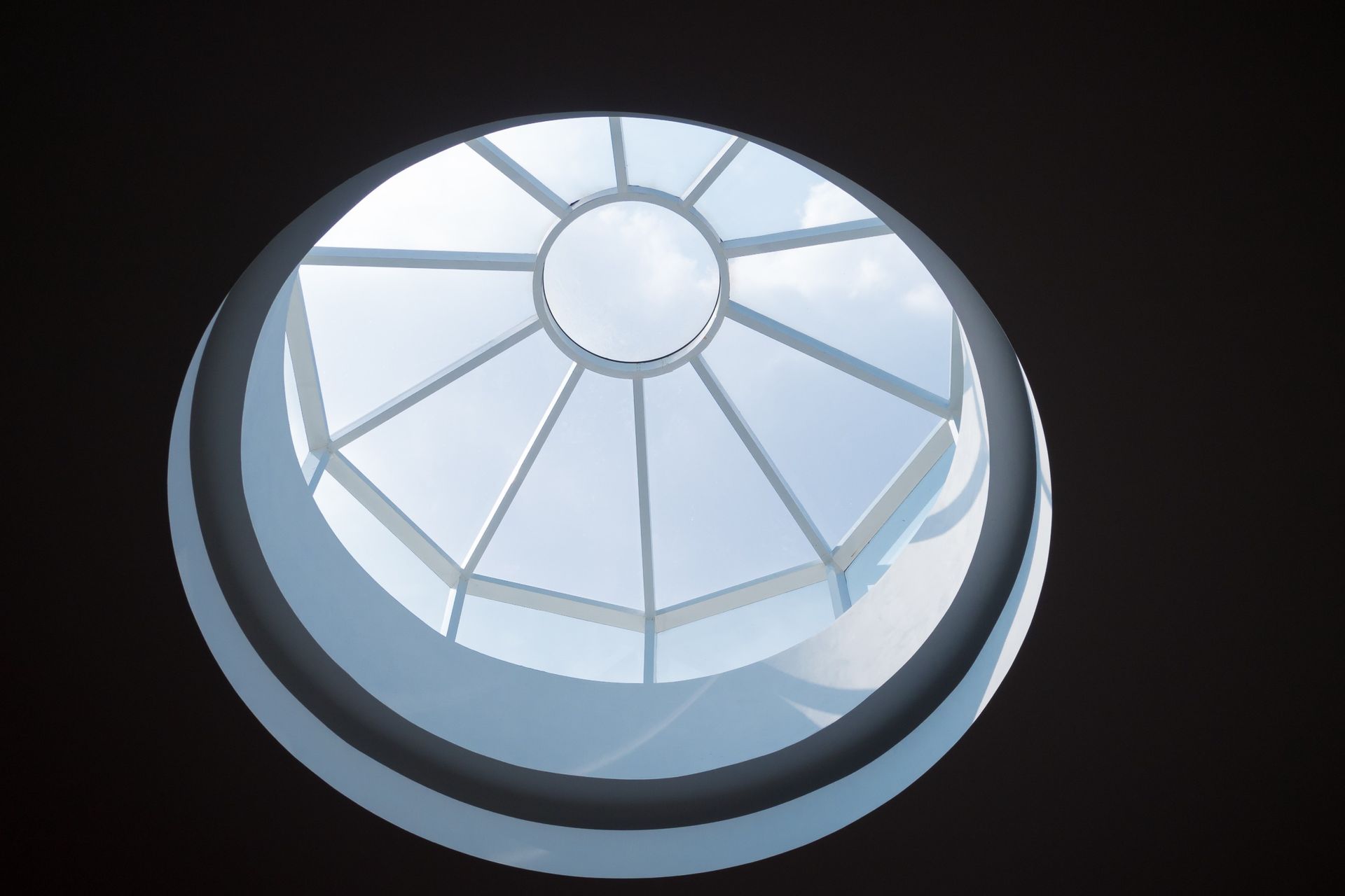 Tragaluz circular con vista a un cielo brillante y parcialmente nublado a través de paneles de vidrio.