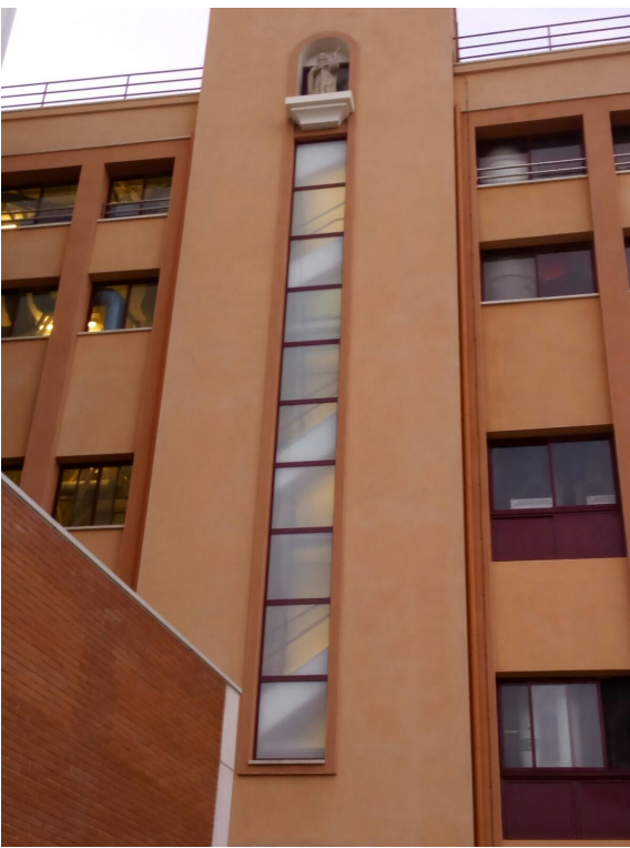 Exterior del edificio, de color melocotón, con una alta vidriera vertical y una estatua.