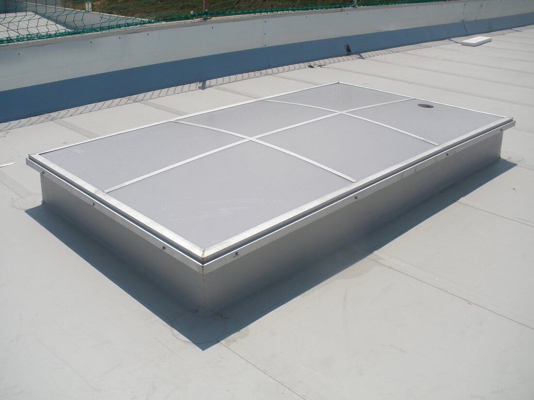 Claraboya rectangular sobre cubierta comercial plana, estructura metálica con paneles.