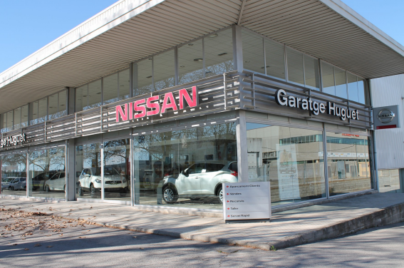 Concesionario de automóviles Nissan con ventanas de cristal y un coche blanco en exposición.