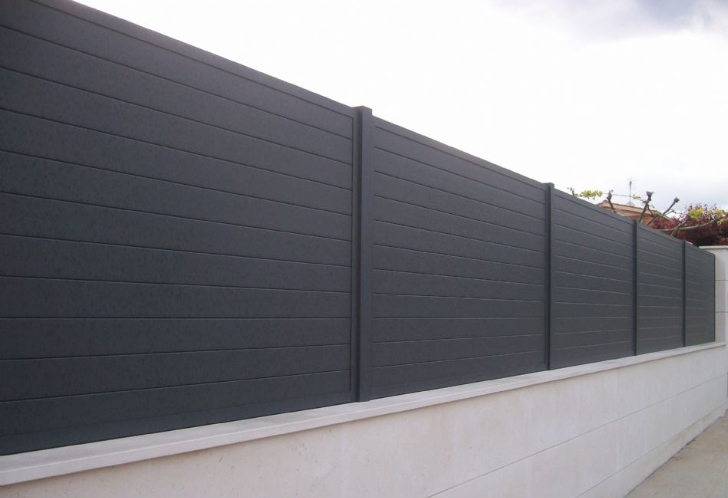 Valla de listones horizontales de color gris oscuro sobre una pared de hormigón blanco.