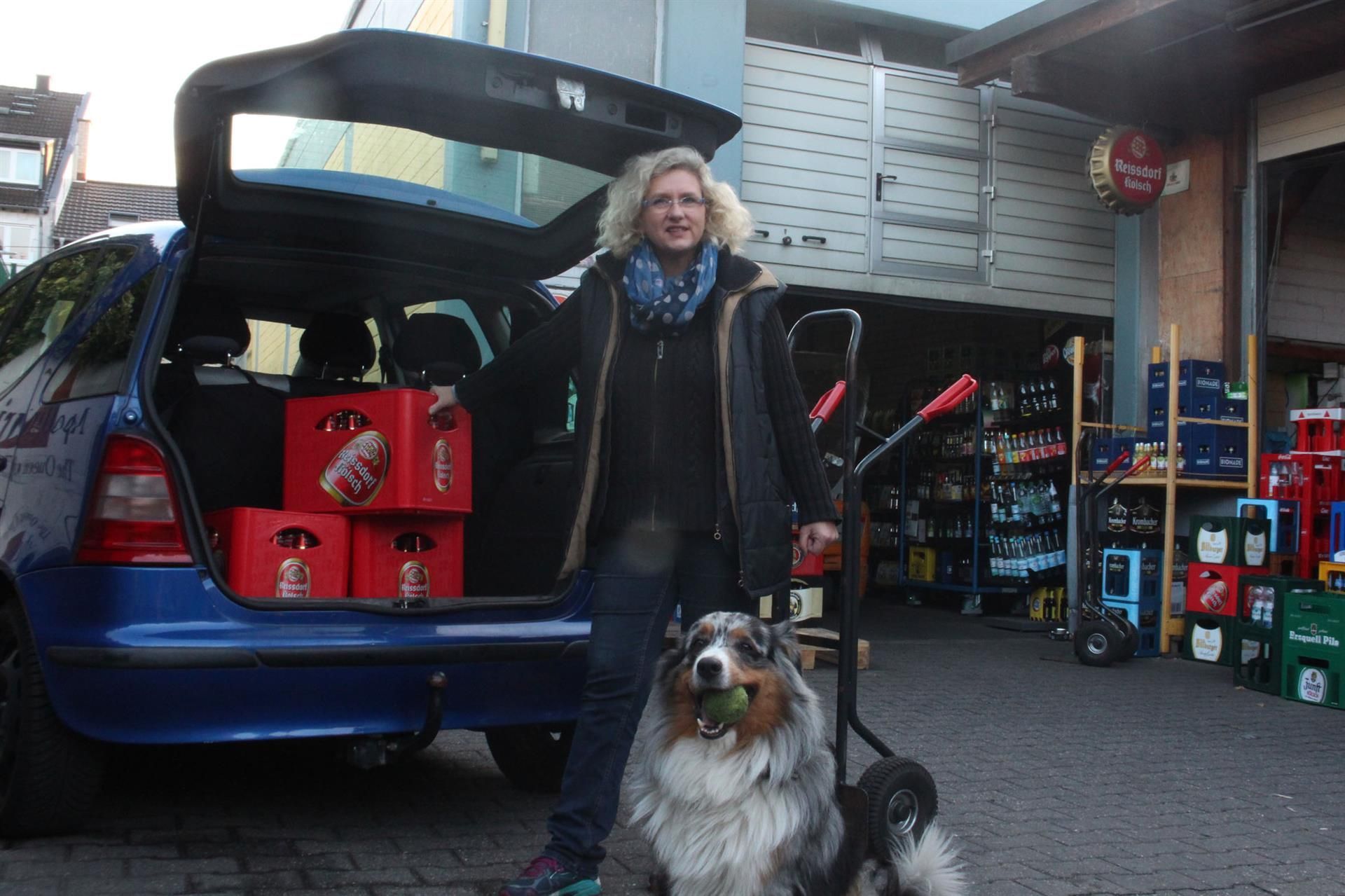 Eine Frau steht neben einem Hund vor einem blauen Auto