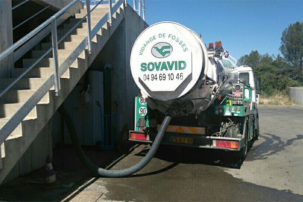 Camion aspirateur Sovavid stationné à côté d'un escalier, avec un tuyau raccordé à une bouche d'égout en bord de route.