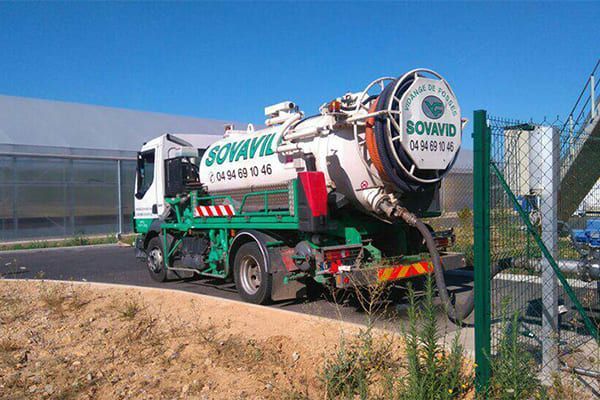 Camion-citerne blanc et vert garé à côté d'une clôture sur un terrain vague sous un ciel bleu