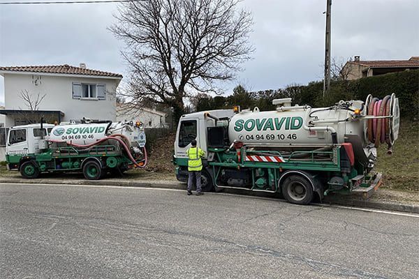Deux camions de service SOVAVID verts dans une rue, avec un employé portant un gilet haute visibilité à proximité.