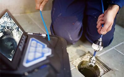 Une personne utilise une caméra d'inspection de canalisation pour examiner un tuyau bouché dans une canalisation carrelée.