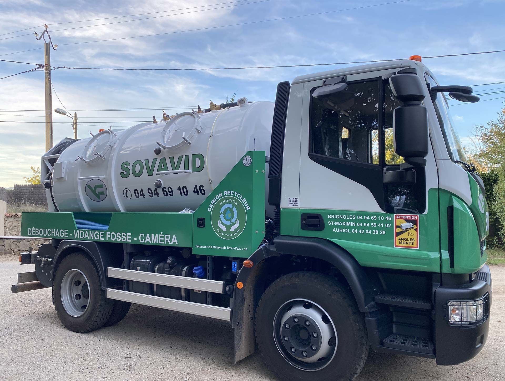 Camion-poubelle SOVAUD vert et blanc stationné à l'extérieur sous un ciel nuageux.