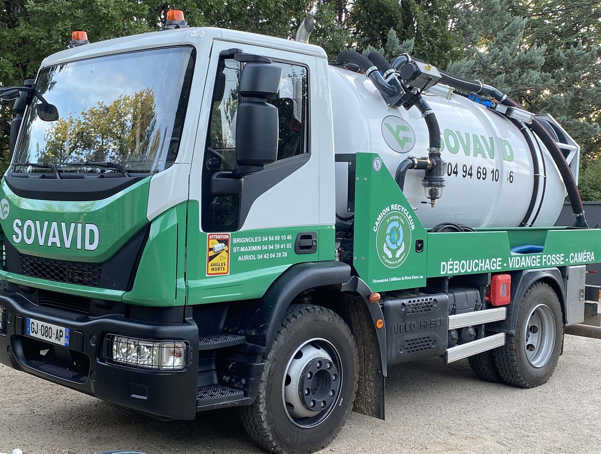 Camion aspirateur SOVID vert et blanc stationné à l'extérieur sur une route de gravier