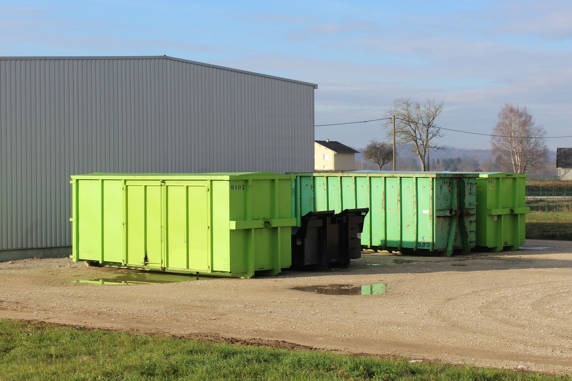 Des conteneurs à déchets verts sont installés à l'extérieur d'un bâtiment en tôle ondulée.
