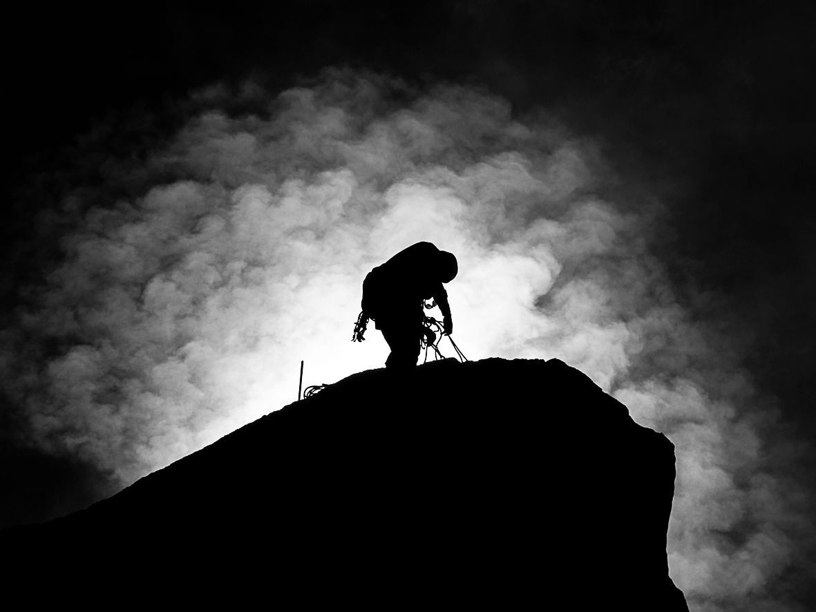 Ombre d'une personne au sommet d'un rocher qu'elle escalade.