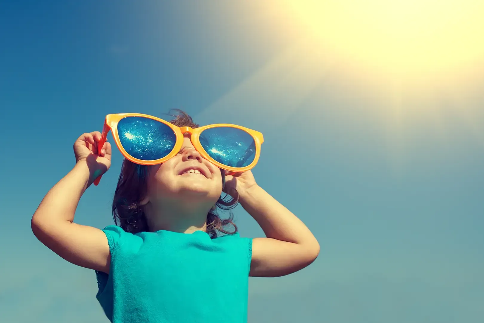 Eine Person mit einer übergroßen gelben Sonnenbrille blickt in eine helle Sonne am klaren blauen Himmel.