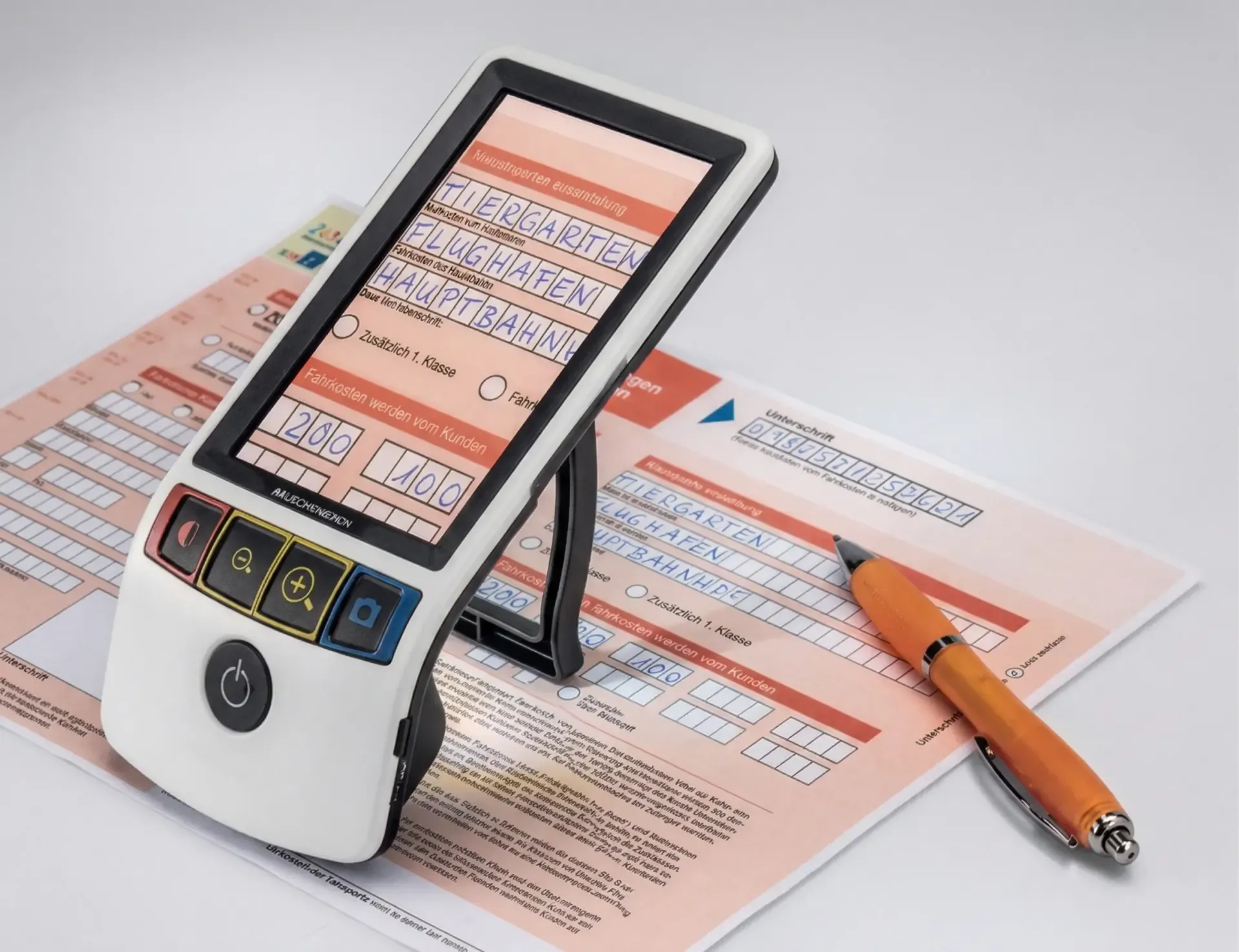 Auf einem Papierformular steht neben einem orangefarbenen Stift eine digitale Videolupe, die den Text des Dokuments auf ihrem Bildschirm vergrößert.