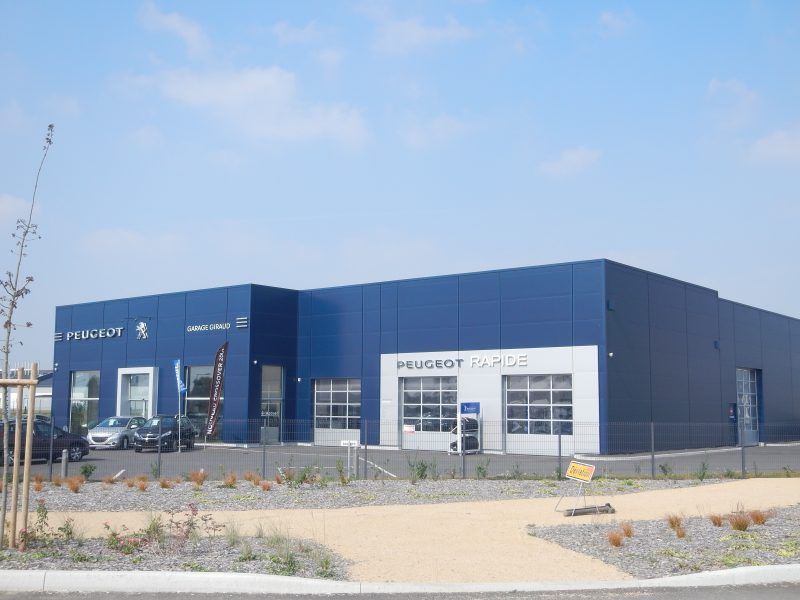 Bâtiment bleu abritant une concession Peugeot, avec des fenêtres en verre et une porte de garage.