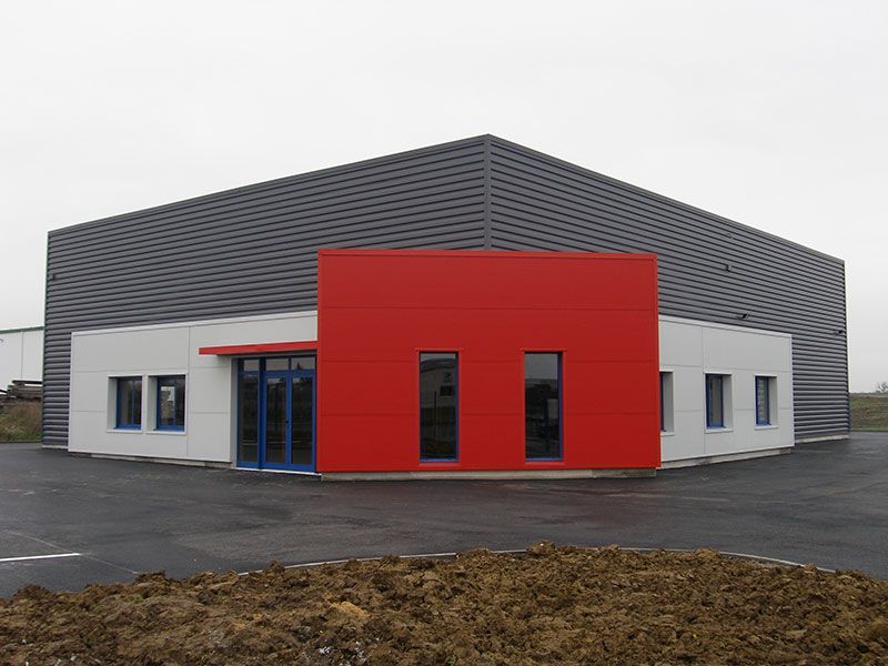 Bâtiment industriel moderne avec façade grise, touches de rouge et petites fenêtres.