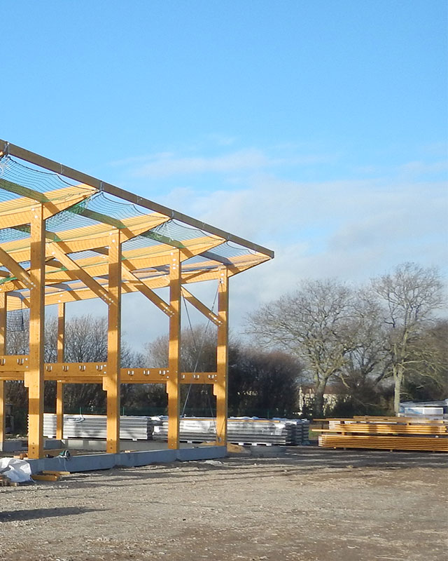 La charpente en bois d'un bâtiment en construction se détache sur un ciel bleu, avec des arbres en arrière-plan.