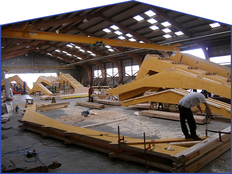 Construction d'une structure en bois à l'intérieur d'un grand entrepôt. Des ouvriers assemblent de grosses poutres.