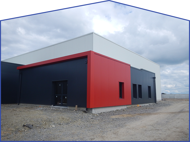 Bâtiment moderne aux murs noirs et rouges, toit blanc, ciel nuageux.