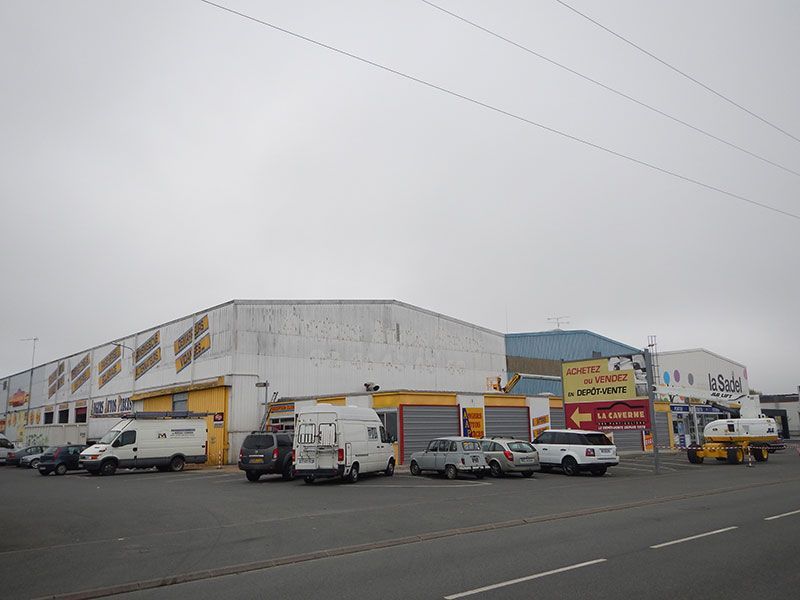 Vue extérieure d'un bâtiment commercial avec des véhicules stationnés devant, sous un ciel nuageux.