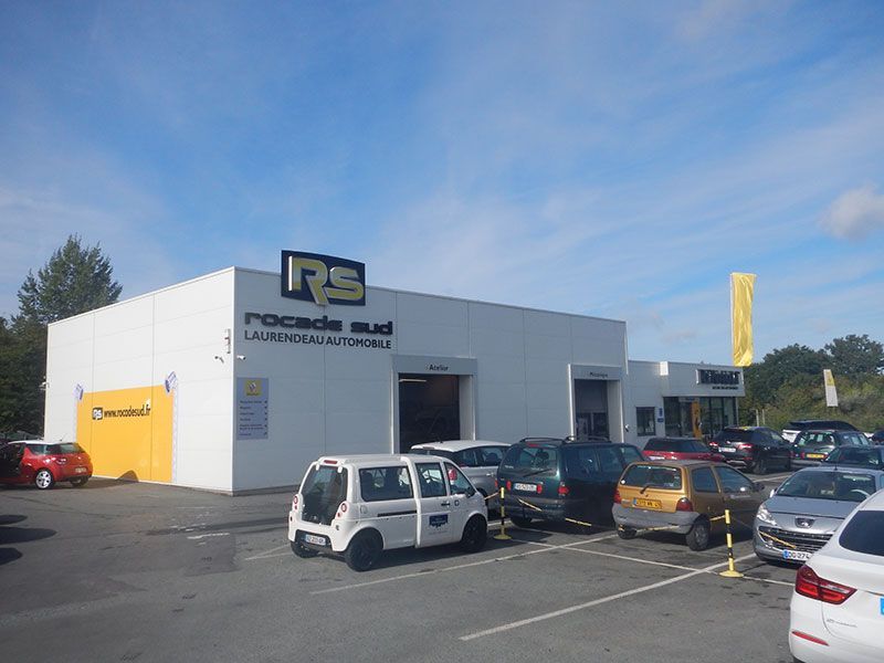 Bâtiment blanc avec l'enseigne RS Rocade Sud, voitures garées devant. Ciel bleu en arrière-plan.