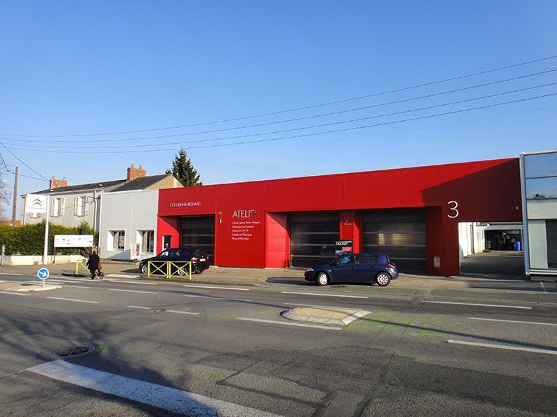 Bâtiment de garage rouge et gris avec portes ouvertes. Voitures garées à l'extérieur.