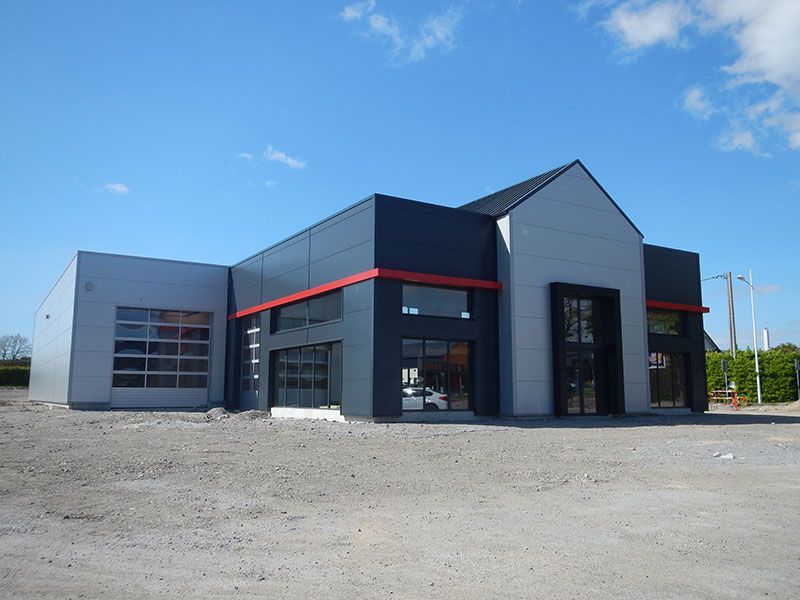 Bâtiment moderne gris et noir avec de grandes fenêtres et une porte de garage sous un ciel bleu.