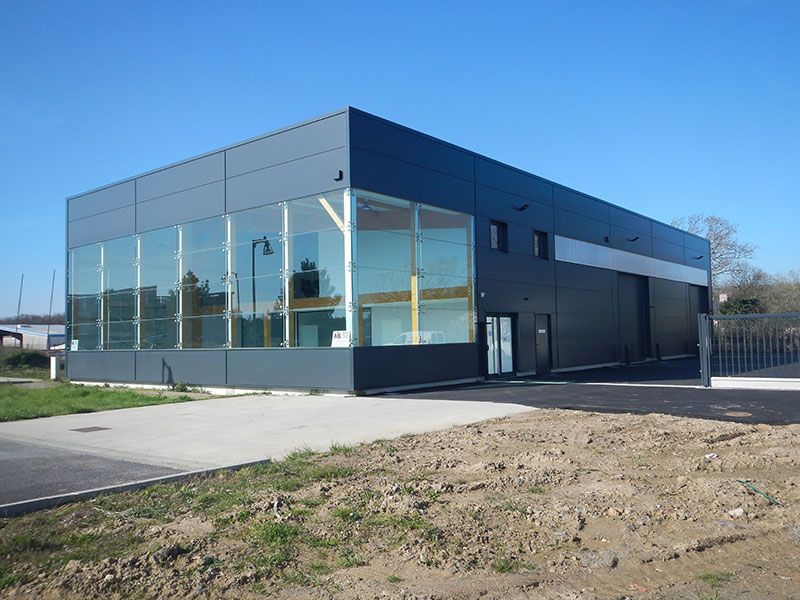 Bâtiment industriel moderne avec de grandes baies vitrées et des panneaux gris foncé se détachant sur un ciel bleu.