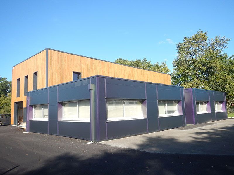 Bâtiment moderne avec des panneaux en bois et gris foncé, des fenêtres et un ciel bleu.