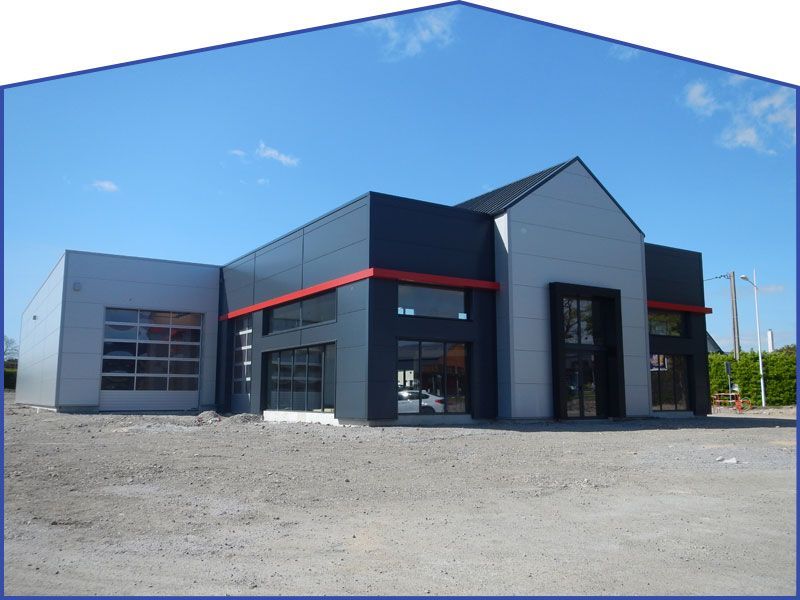 Bâtiment moderne à l'extérieur gris et noir, avec des touches de rouge et des portes de garage vitrées, sous un ciel bleu.