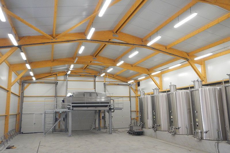 Intérieur d'un grand entrepôt avec poutres en bois, réservoirs en acier inoxydable et machines industrielles.