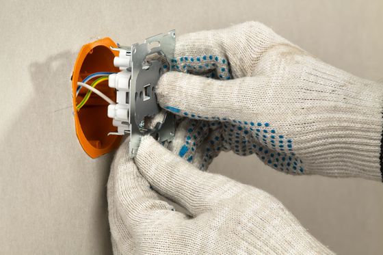 Des mains gantées installent une prise électrique murale.