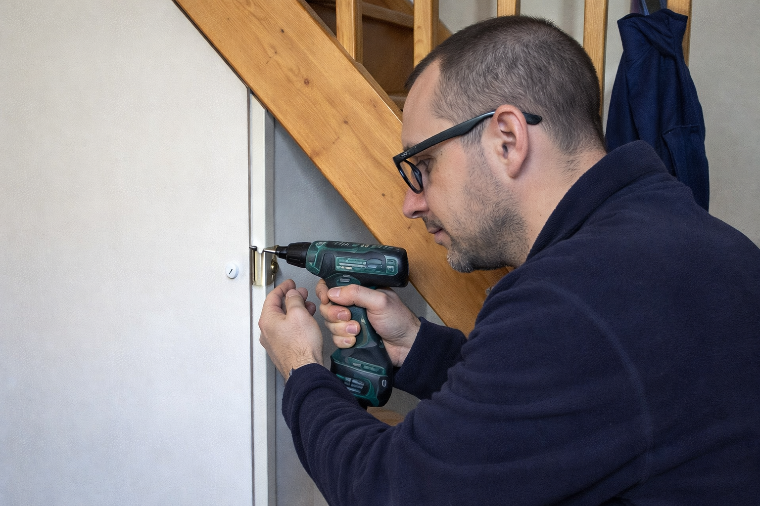 Une personne utilise une perceuse sans fil pour fixer une charnière métallique sur un cadre de porte blanc.
