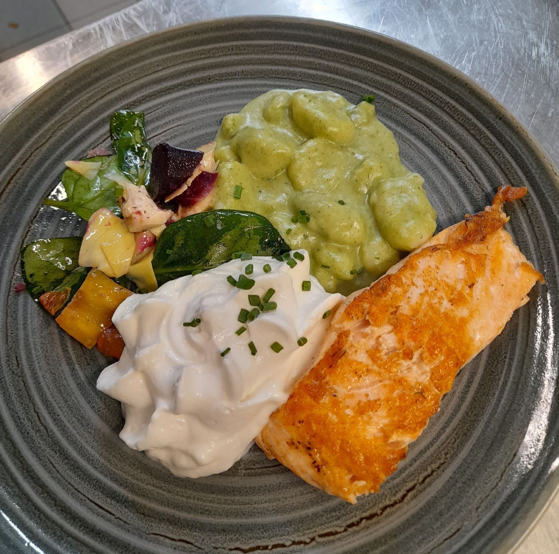 Saumon servi avec une sauce crémeuse, des gnocchis et des légumes rôtis dans un plat gris.