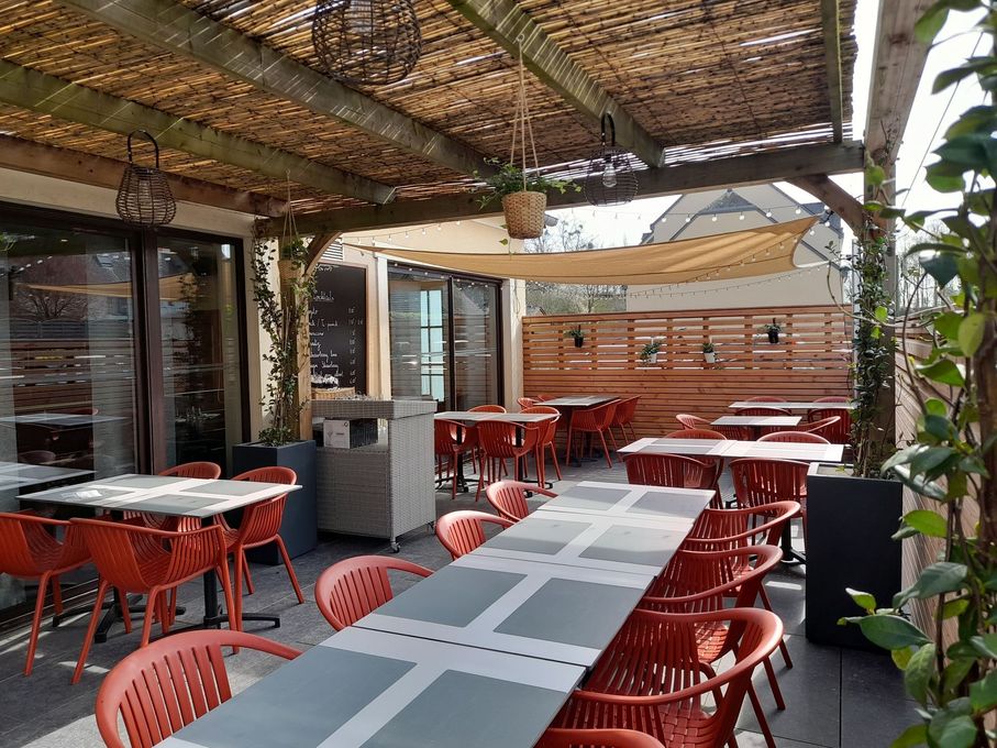 Terrasse de café en plein air avec chaises rouges, tables grises et plafond couvert d'un auvent ombragé