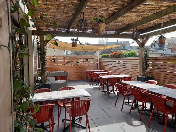 Terrasse de café en plein air vide, avec chaises rouges, tables blanches et toit en bambou ombragé