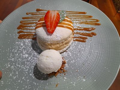 Assiette de dessert avec une pâtisserie garnie de fraises, une boule de vanille et un filet de caramel.