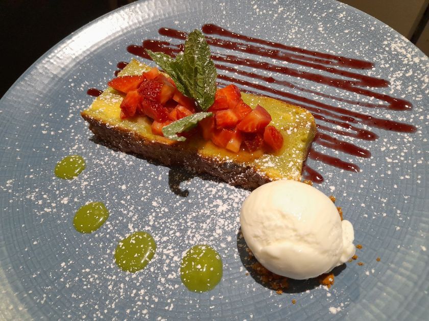 Assiette de dessert composée d'une pâtisserie nappée de caramel, de fruits coupés en dés, de points de sauce verte et d'une boule de glace à la vanille.