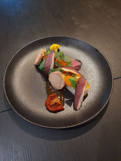 Plat gastronomique composé de viande tranchée, de légumes et de sauce, présenté sur une table sombre.