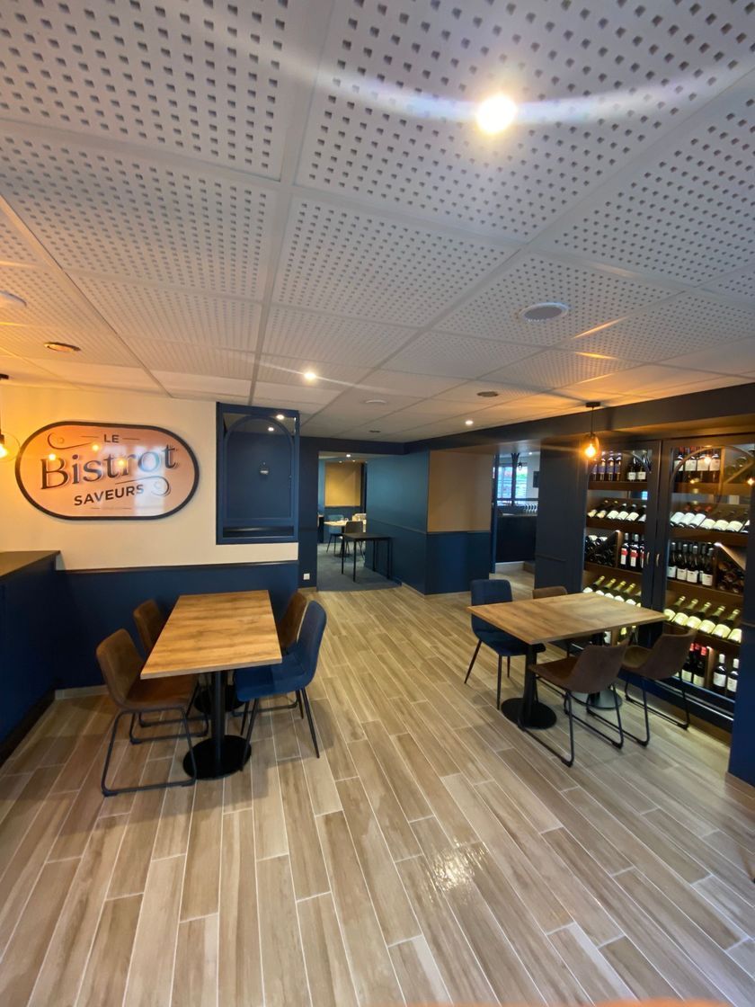 Café moderne vide avec tables en bois, murs bleus et présentoir à bouteilles sur le côté droit.
