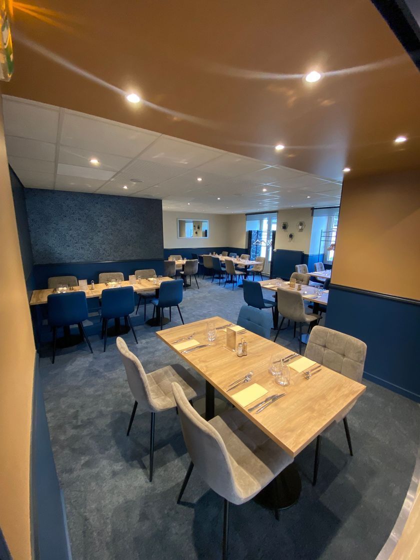 Salle à manger de restaurant moderne avec chaises bleues, tables en bois et éclairage chaleureux au plafond.