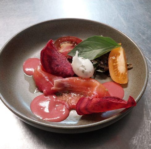 Salade gourmande dressée à l'assiette, composée de tranches de tomates, de betteraves, de verdure et d'une sauce rose crémeuse, le tout servi dans un plat gris.